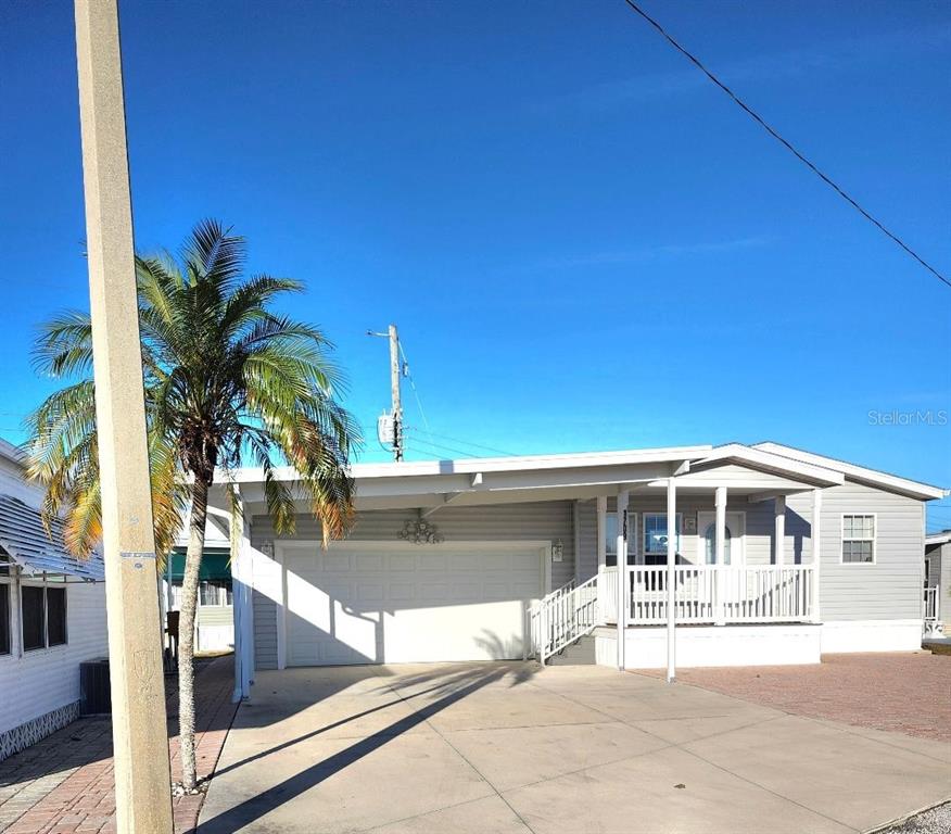 A light gray manufactured home features a white garage door, a covered porch, and palm trees — 1709 MINNESOTA AVENUE, BRADENTON, FL
