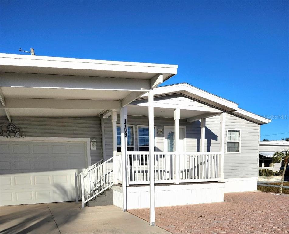 A light gray manufactured home features a covered carport, a front porch, and a driveway — 1709 MINNESOTA AVENUE, BRADENTON, FL