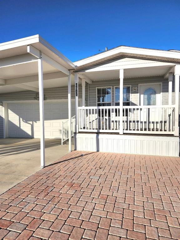 A manufactured home features a covered carport, a front porch, and a brick paver driveway — 1709 MINNESOTA AVENUE, BRADENTON, FL