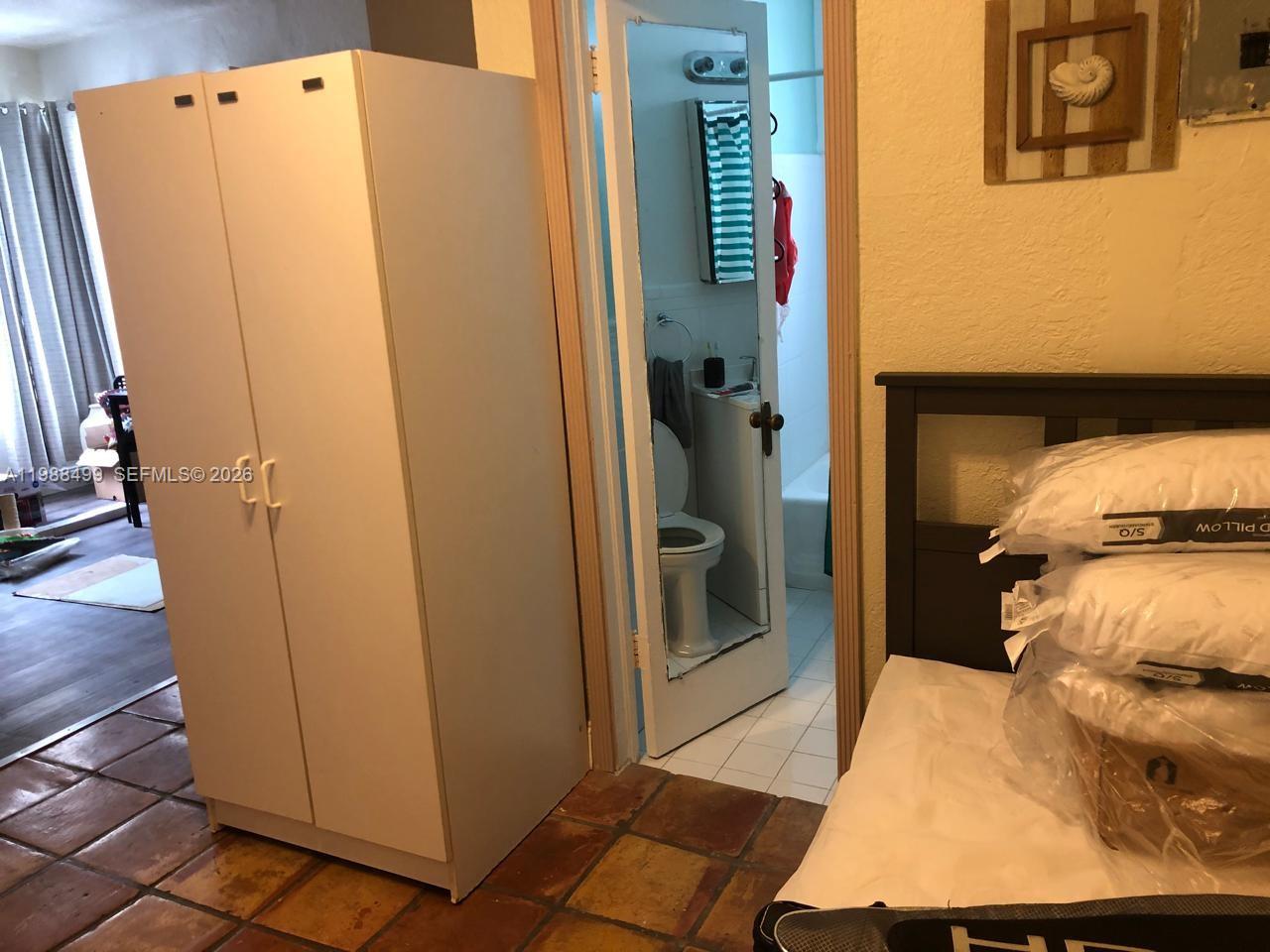 A bedroom features a white wardrobe, a bed with packaged pillows, and an adjacent bathroom — 3710 Collins Ave # 310, Miami Beach FL 33140, MIAMI BEACH, FL