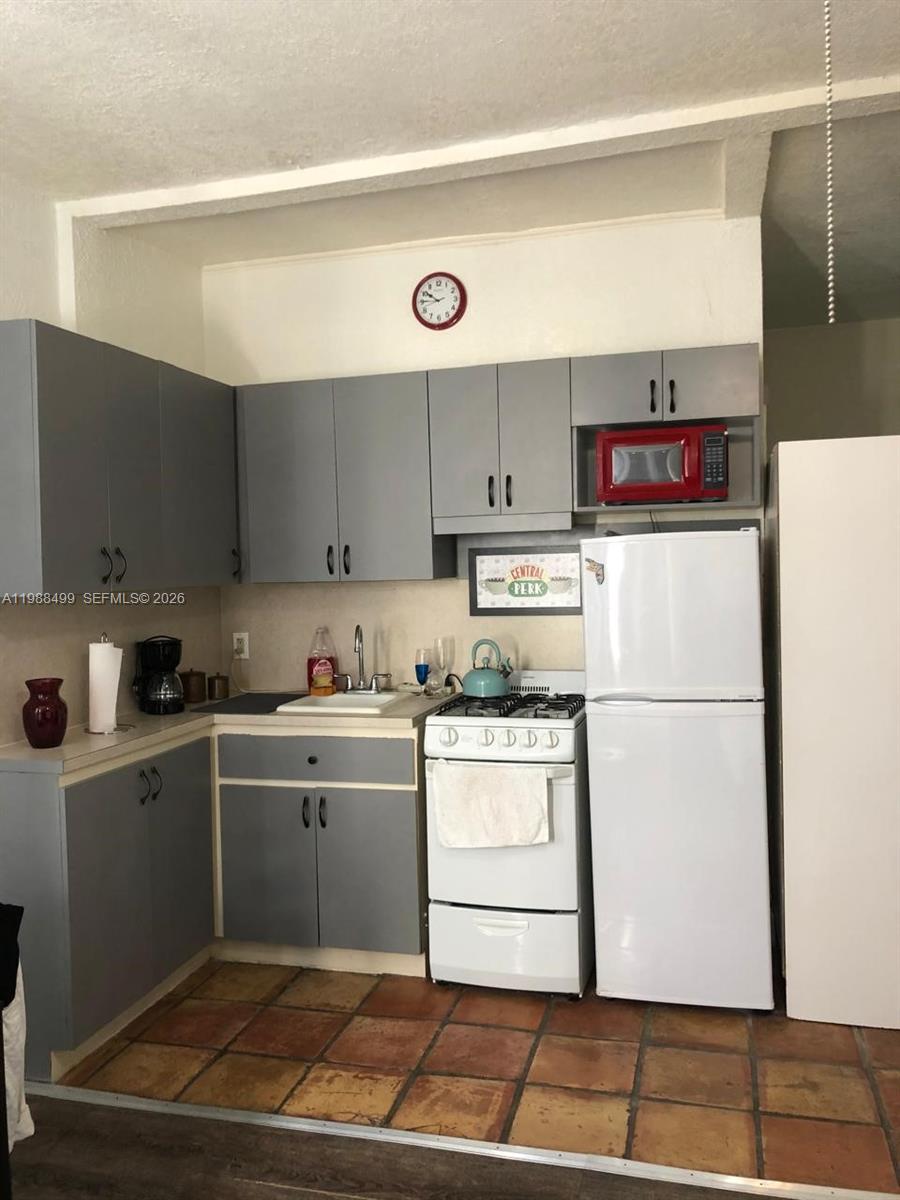A kitchen features gray cabinets, a white stove, a white refrigerator, and tiled flooring — 3710 Collins Ave # 310, Miami Beach FL 33140, MIAMI BEACH, FL