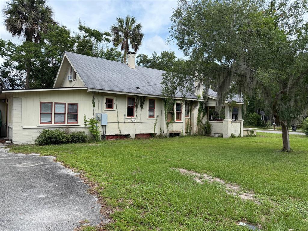 A side view of a one-story house with light-colored siding, a gray roof, and landscaping — 528 N ADELLE AVENUE, DELAND, FL