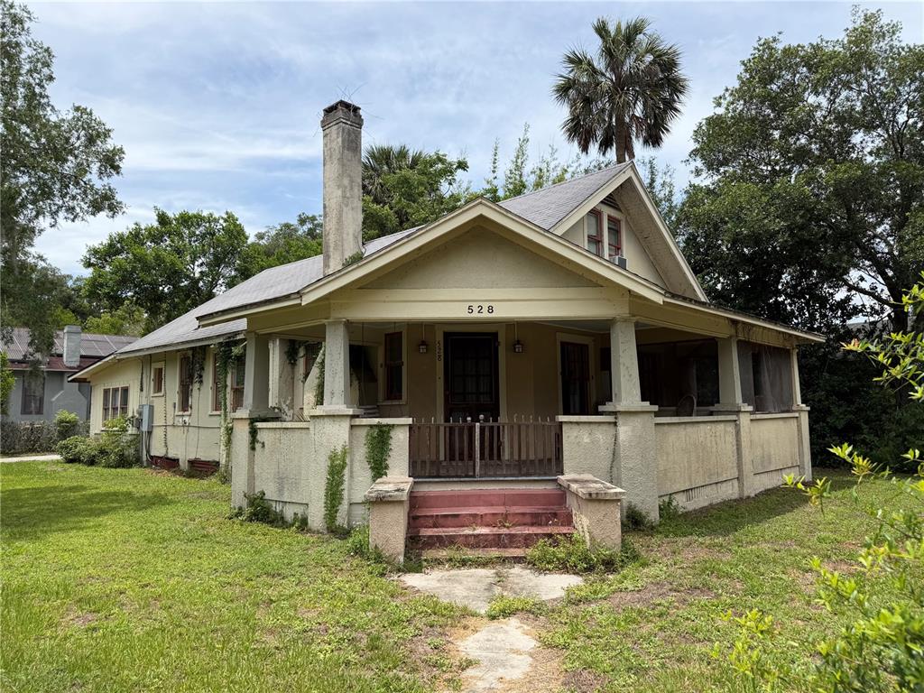 A single-story house with a wrap-around porch, stucco siding, and a prominent brick chimney — 528 N ADELLE AVENUE, DELAND, FL