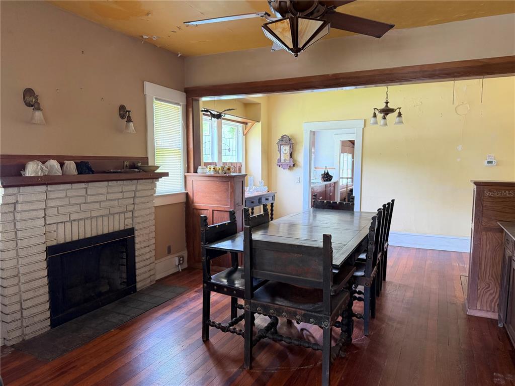 A dining room with a brick fireplace, wooden floors, and a dark wood table set — 528 N ADELLE AVENUE, DELAND, FL