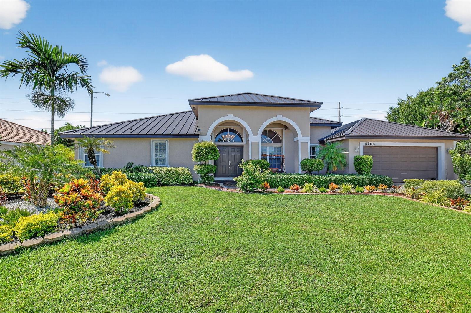 A single-story house with a dark metal roof, arched entryway, and landscaped front lawn — 4768 Cypress Drive S, Boynton Beach FL 33436, BOYNTON BEACH, FL