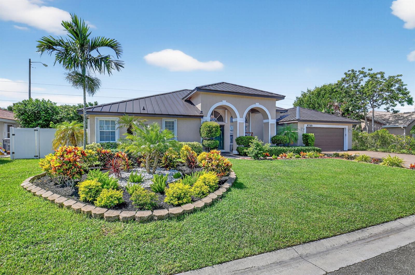 A single-story house with a metal roof, arched entryway, and a landscaped front garden — 4768 Cypress Drive S, Boynton Beach FL 33436, BOYNTON BEACH, FL