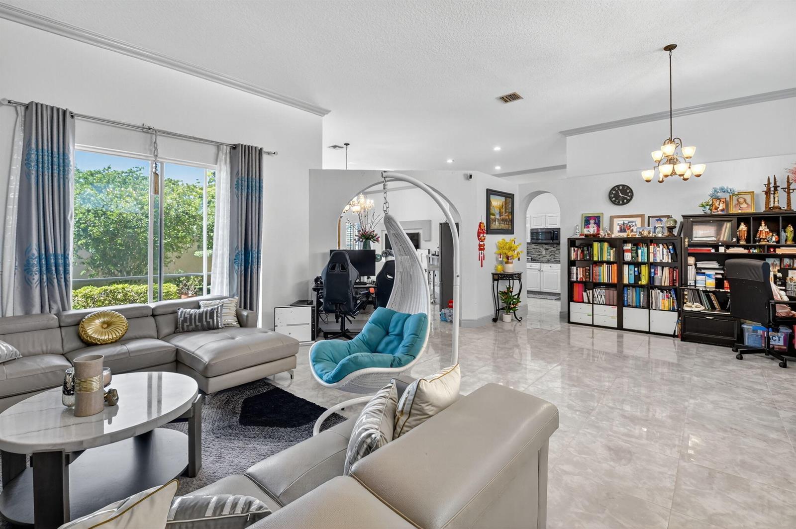 A living room features a grey sectional sofa, a hanging chair, and a large bookshelf — 4768 Cypress Drive S, Boynton Beach FL 33436, BOYNTON BEACH, FL