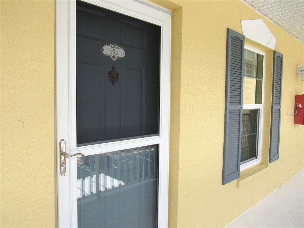 A white storm door with the number 933 leads into a yellow-walled building exterior — 175 KINGS HIGHWAY UNIT 933, PUNTA GORDA, FL