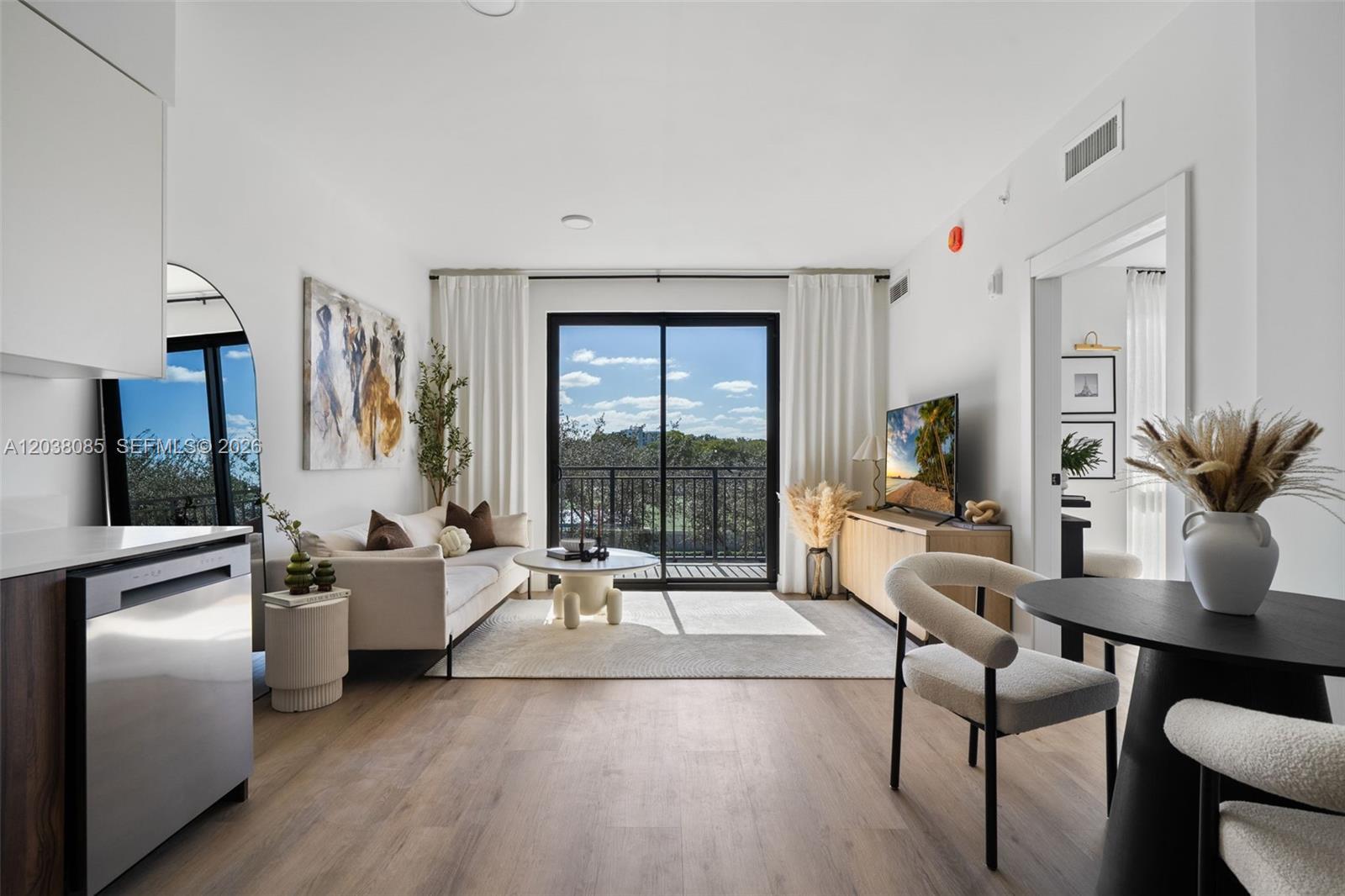 A modern living room features wood flooring, a neutral sofa, and a balcony with greenery — 2479 NE 192nd St # 306, Miami FL 33180, MIAMI, FL