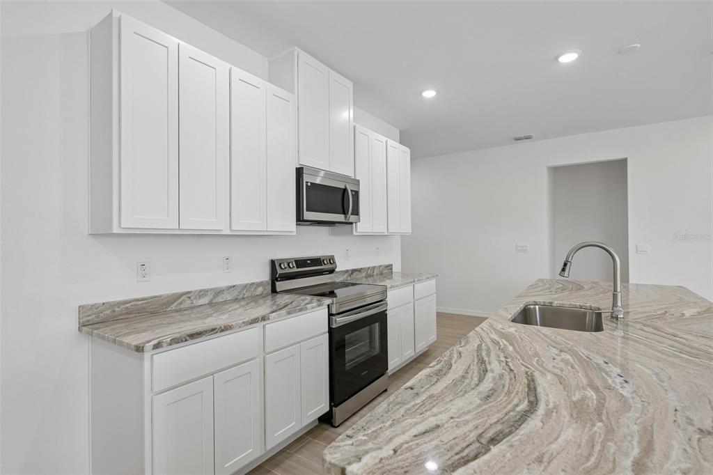 A modern kitchen features white cabinets, stainless steel appliances, and a large stone-topped island — 22500 PROVANCE AVENUE, PORT CHARLOTTE, FL