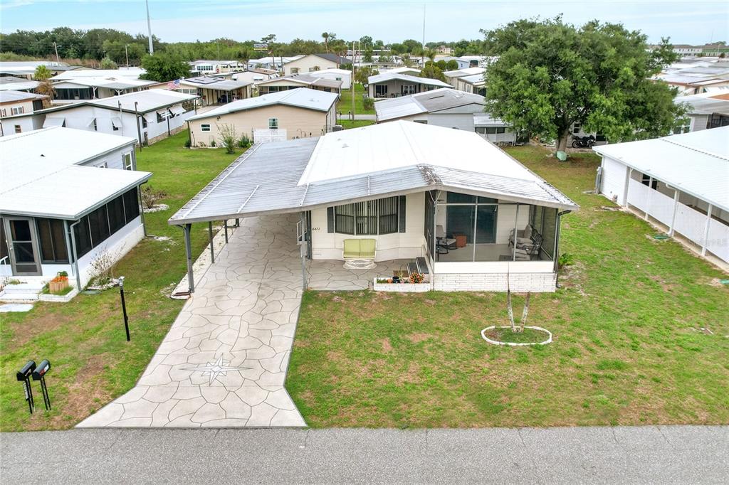 An aerial view of a manufactured home with a carport, screened porch, and paved driveway — 6473 PEPPERTREE PATH NE, WINTER HAVEN, FL