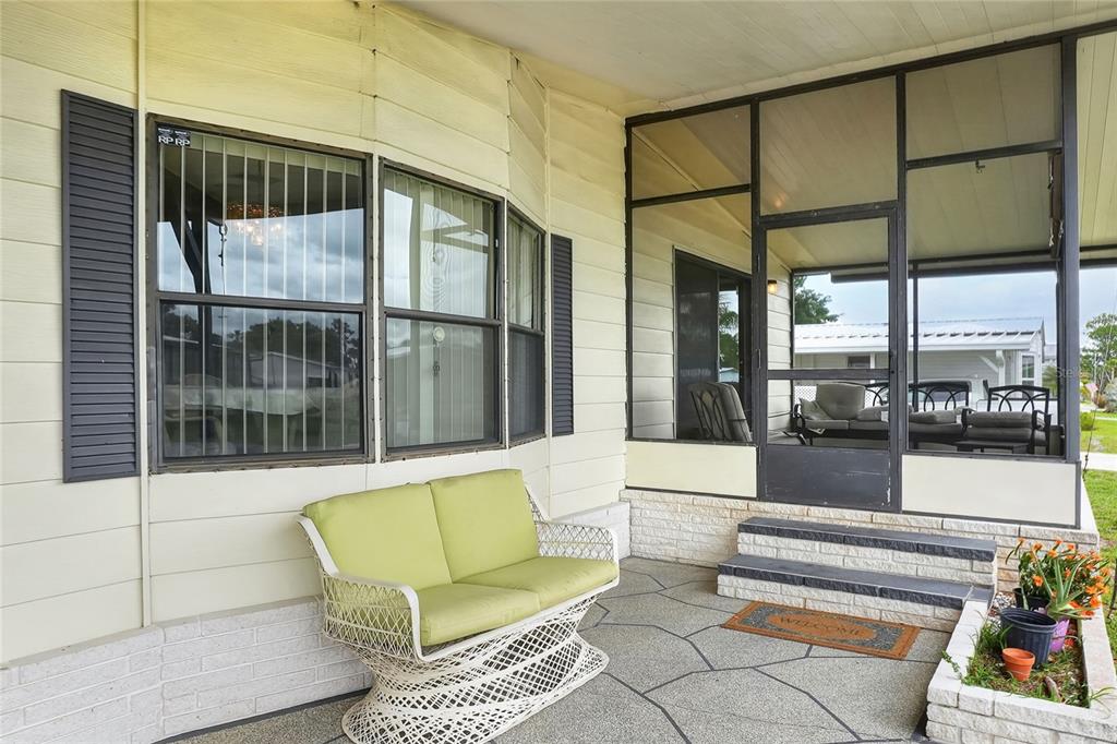 A covered porch features a white wicker loveseat, a screened-in area, and stone-patterned flooring — 6473 PEPPERTREE PATH NE, WINTER HAVEN, FL