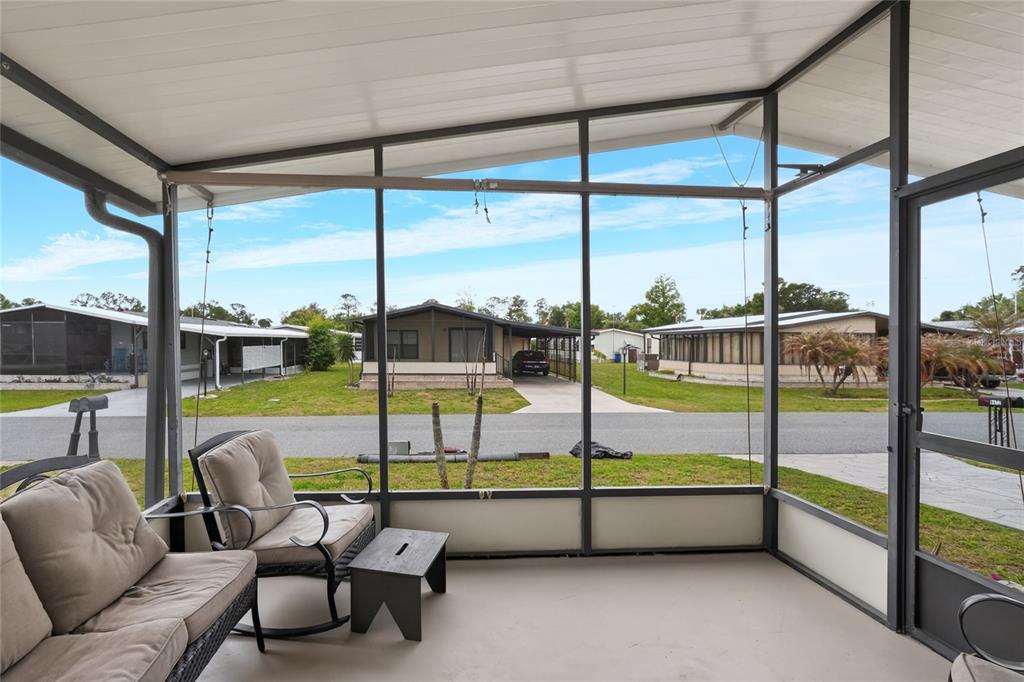A screened-in porch with outdoor furniture overlooks a residential street with several manufactured homes — 6473 PEPPERTREE PATH NE, WINTER HAVEN, FL
