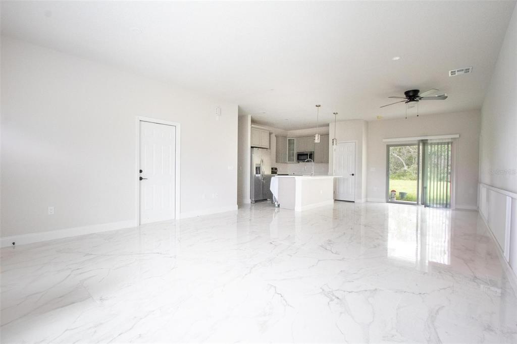 An open-concept living area features white marble-look tile flooring and a kitchen with white cabinetry — 301 BOWFIN DRIVE, KISSIMMEE, FL