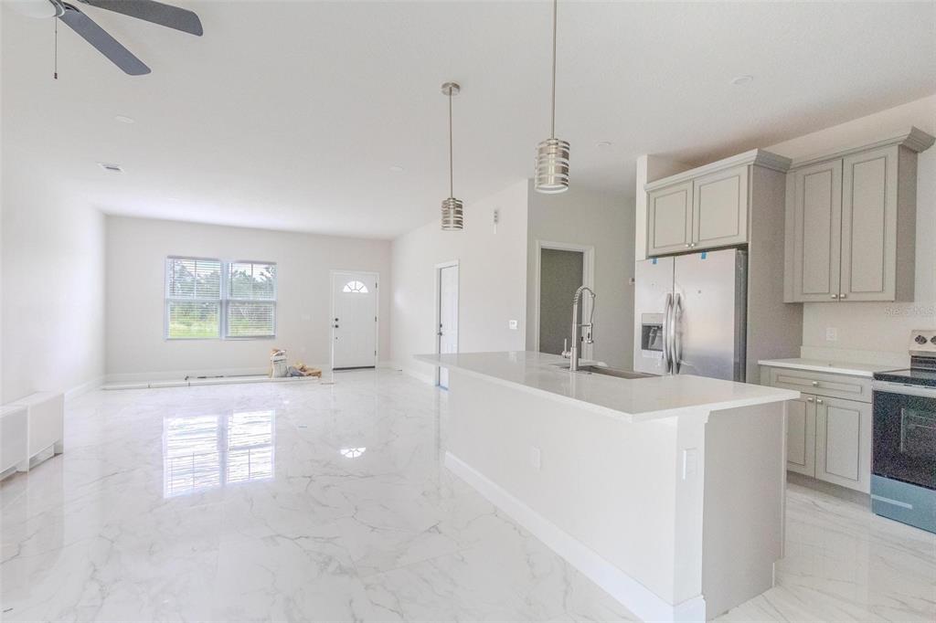 An open-concept kitchen and living area features white marble-look tile flooring and gray cabinetry — 301 BOWFIN DRIVE, KISSIMMEE, FL