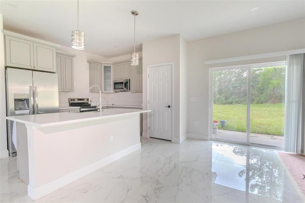 A modern kitchen features white cabinets, stainless steel appliances, a quartz island, and marble-look flooring — 301 BOWFIN DRIVE, KISSIMMEE, FL