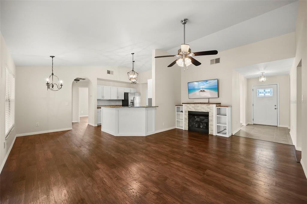 An open-concept living room and kitchen featuring hardwood floors, a fireplace, and a ceiling fan — 14513 POINTE EAST TRAIL, CLERMONT, FL