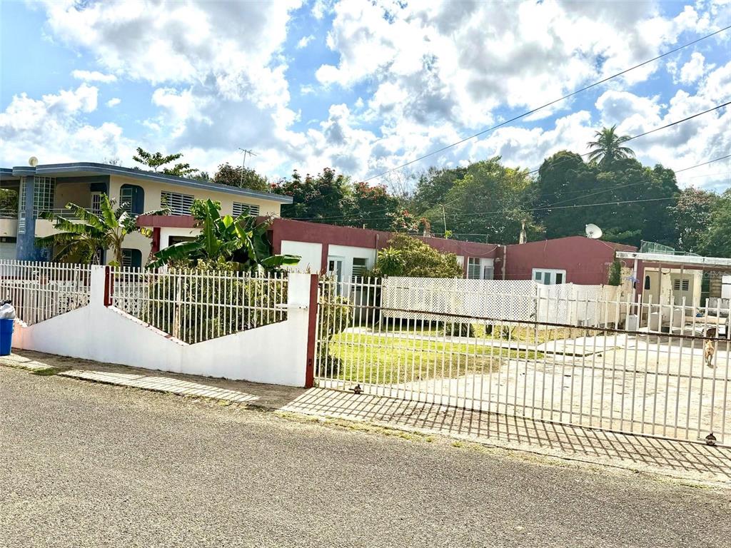 A two-story house with a white metal fence and gate sits behind a paved street — 507 VICENTA ARROYO, MANATI, PR