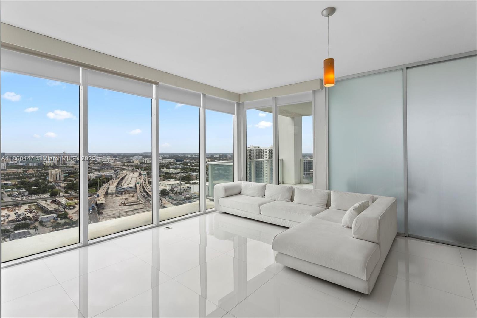 A modern living room features white tile floors, a sectional sofa, and floor-to-ceiling windows — 1040 Biscayne Blvd # 3106, Miami FL 33132, MIAMI, FL