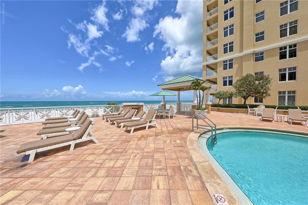 A pool deck with lounge chairs overlooks the ocean next to a multi-story building — 10 PAPAYA STREET UNIT 305, CLEARWATER BEACH, FL