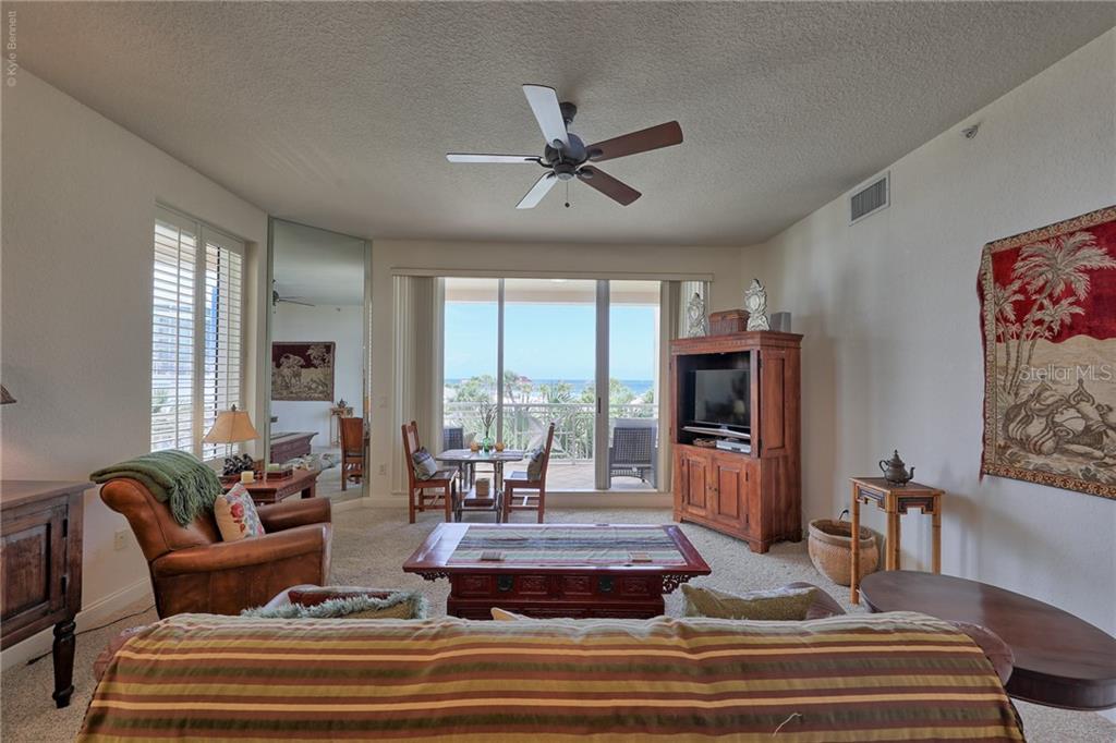 A living room features a ceiling fan, a wooden entertainment center, and a balcony view — 10 PAPAYA STREET UNIT 305, CLEARWATER BEACH, FL