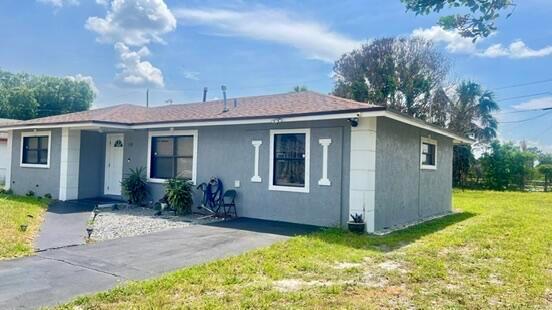 A gray, single-story house with white trim and a shingled roof sits on a lawn — 113 Hilton Drive, Fort Pierce FL 34946, FORT PIERCE, FL