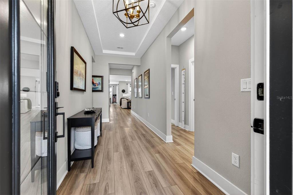A bright hallway features light wood-look flooring, gray walls, and a modern geometric light fixture — 3709 SAVANNA PALMS COURT, BRADENTON, FL