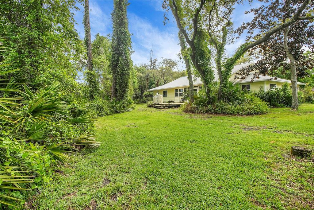 A yellow house with a wooden deck sits in a grassy yard surrounded by trees — 335 RIVER GLASS COURT, LEESBURG, FL