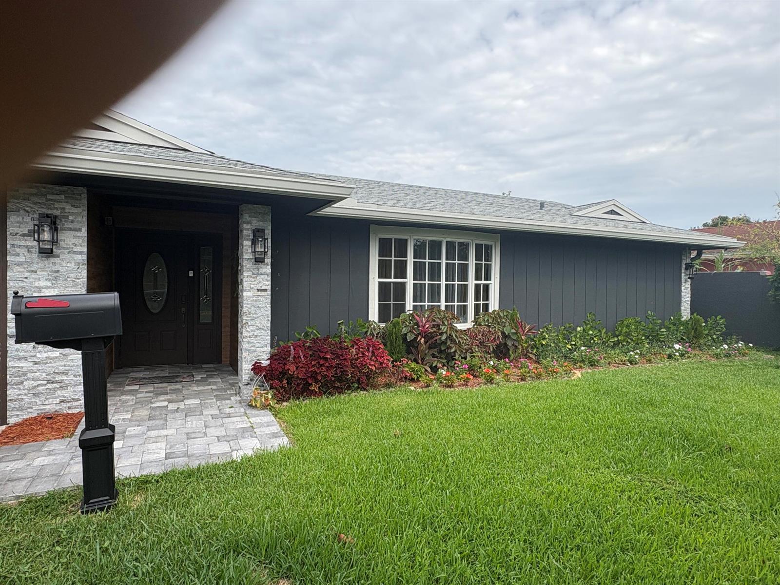 A dark gray house exterior features a stone-accented entryway, a large window, and landscaping — 3501 Boulevard Boulevard, Delray Beach FL 33445, DELRAY BEACH, FL