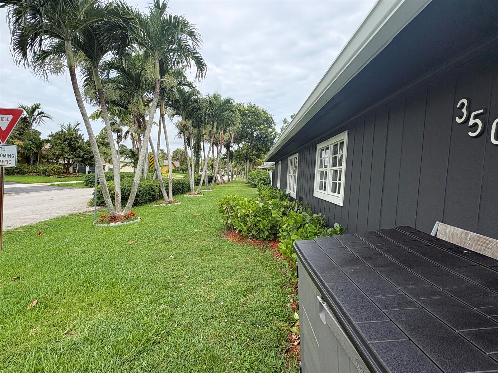 A dark gray house exterior features white-trimmed windows, a storage bin, and palm trees nearby — 3501 Boulevard Boulevard, Delray Beach FL 33445, DELRAY BEACH, FL
