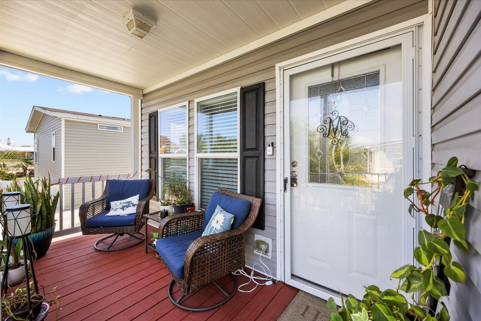 A covered porch with red decking features two wicker chairs and a white front door — 82 Sandhill Boulevard, Fort Pierce FL 34982, FORT PIERCE, FL