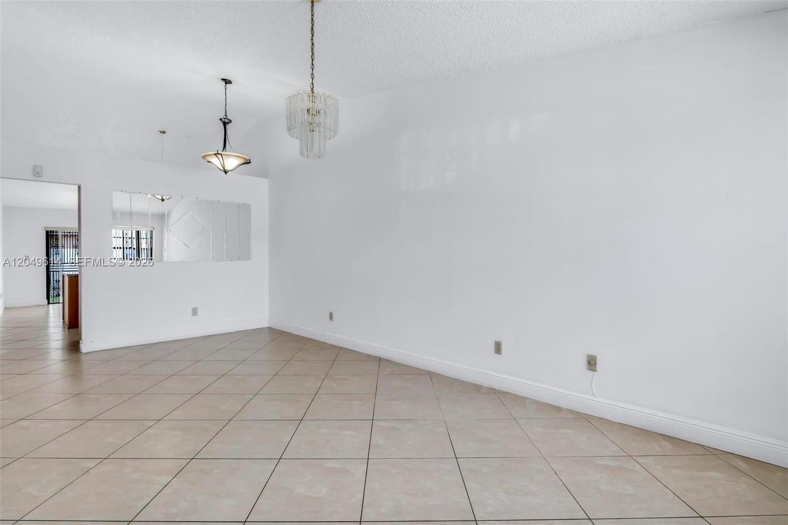 An empty room features white walls, beige tile flooring, and two hanging light fixtures — 8871 NW 114th St, Hialeah Gardens FL 33018, HIALEAH GARDENS, FL