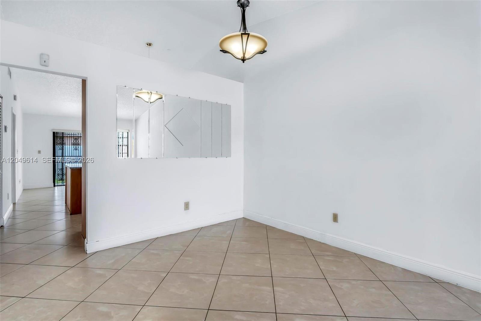 An empty dining area features beige tile flooring, a decorative wall mirror, and a pendant light — 8871 NW 114th St, Hialeah Gardens FL 33018, HIALEAH GARDENS, FL