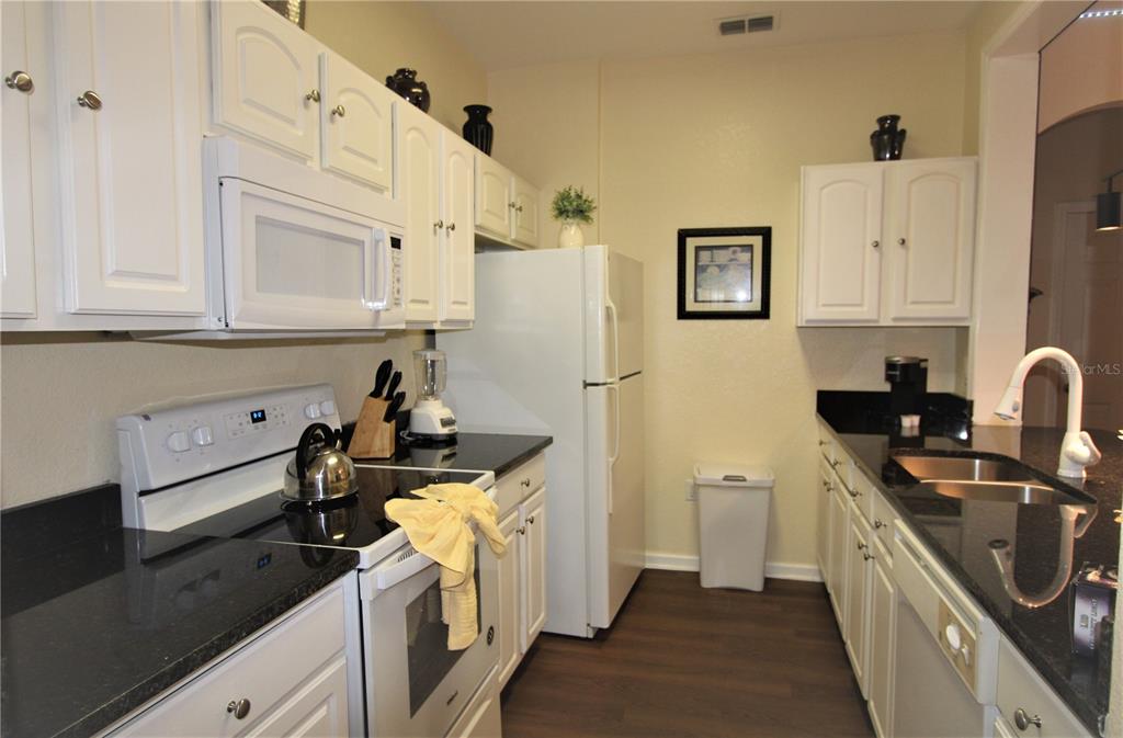 A kitchen features white cabinets, black countertops, white appliances, and dark wood-look flooring — 7671 COMROW STREET UNIT 302, KISSIMMEE, FL