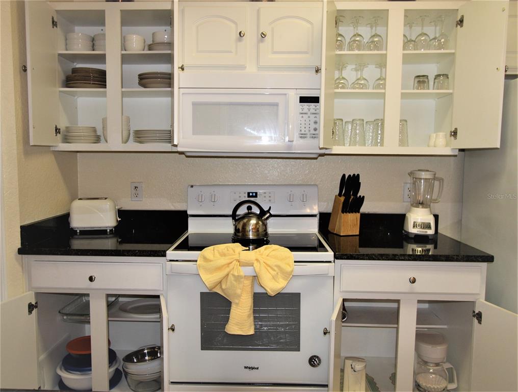 A kitchen features white cabinets, black countertops, a white stove, and a microwave — 7671 COMROW STREET UNIT 302, KISSIMMEE, FL