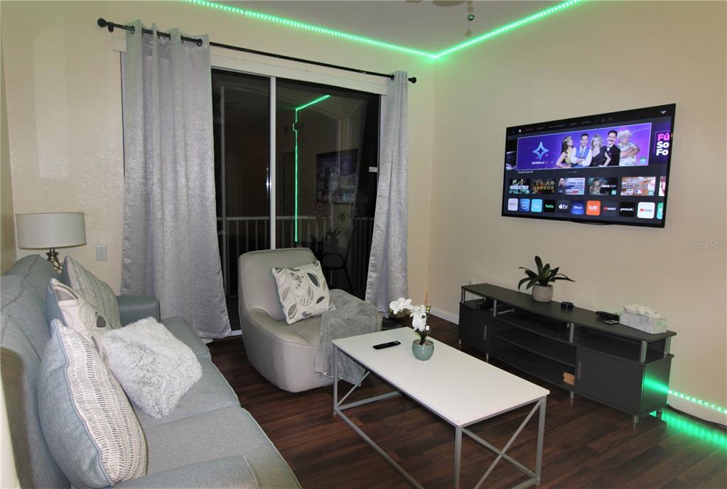 A living room features a grey sofa, a white coffee table, and a wall-mounted television — 7671 COMROW STREET UNIT 302, KISSIMMEE, FL