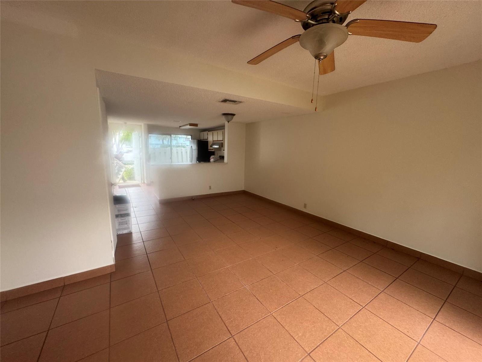 An empty living area with brown tile flooring, a ceiling fan, and an adjacent kitchen — 2845 NE 15th Street, Pompano Beach FL 33062, POMPANO BEACH, FL