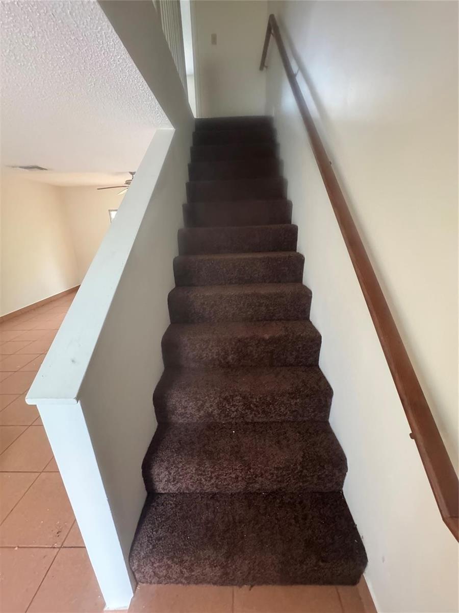 A straight staircase with dark brown carpet and a wooden handrail leads to a landing — 2845 NE 15th Street, Pompano Beach FL 33062, POMPANO BEACH, FL
