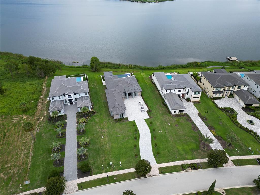 An aerial view shows three modern houses with pools situated along a large lake — 15125 PENDIO DRIVE, MONTVERDE, FL