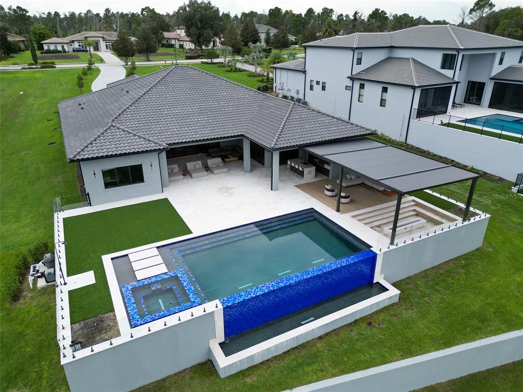 An aerial view of a modern house backyard featuring an infinity pool and covered patio — 15125 PENDIO DRIVE, MONTVERDE, FL