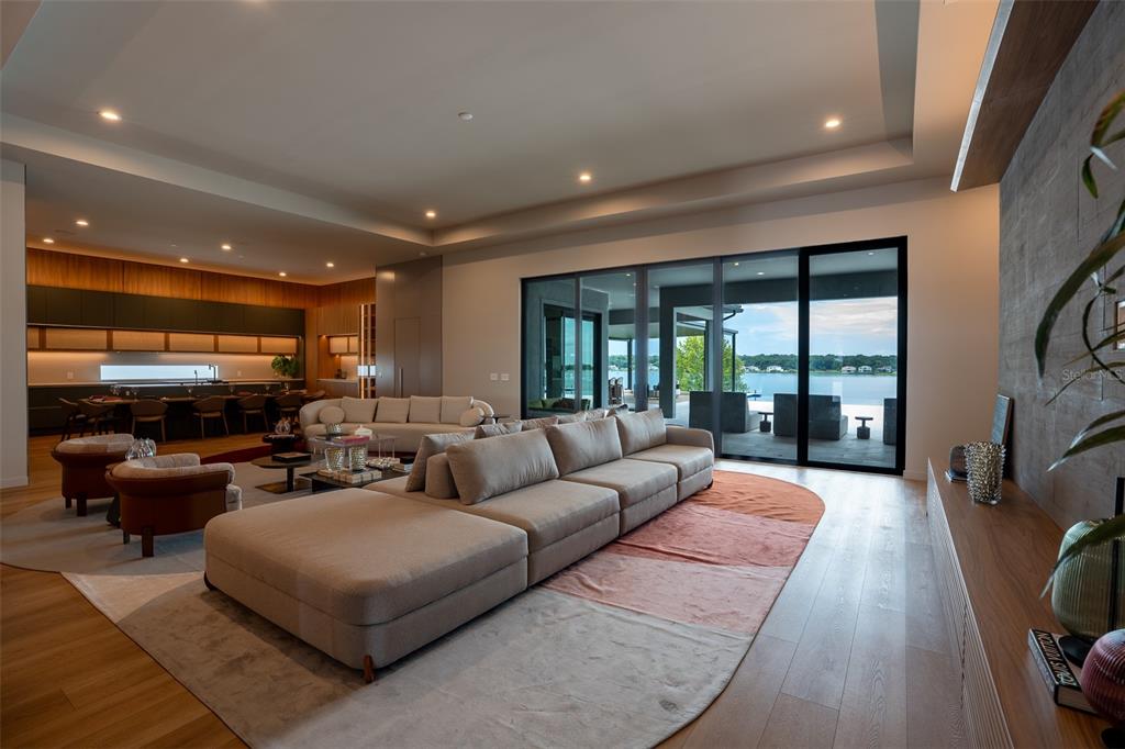 A modern open-concept living room features a large sectional sofa, wood floors, and lake views — 15125 PENDIO DRIVE, MONTVERDE, FL