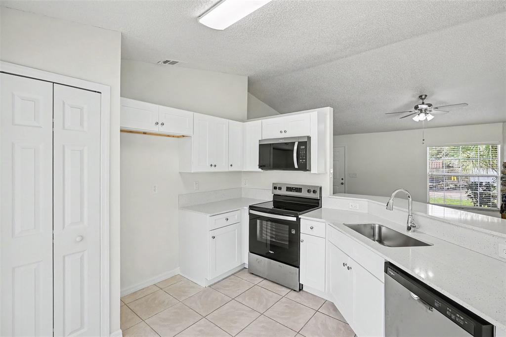 A kitchen features white cabinetry, stainless steel appliances, quartz countertops, and light-colored tile flooring — 6236 BRANDT STREET, COCOA, FL