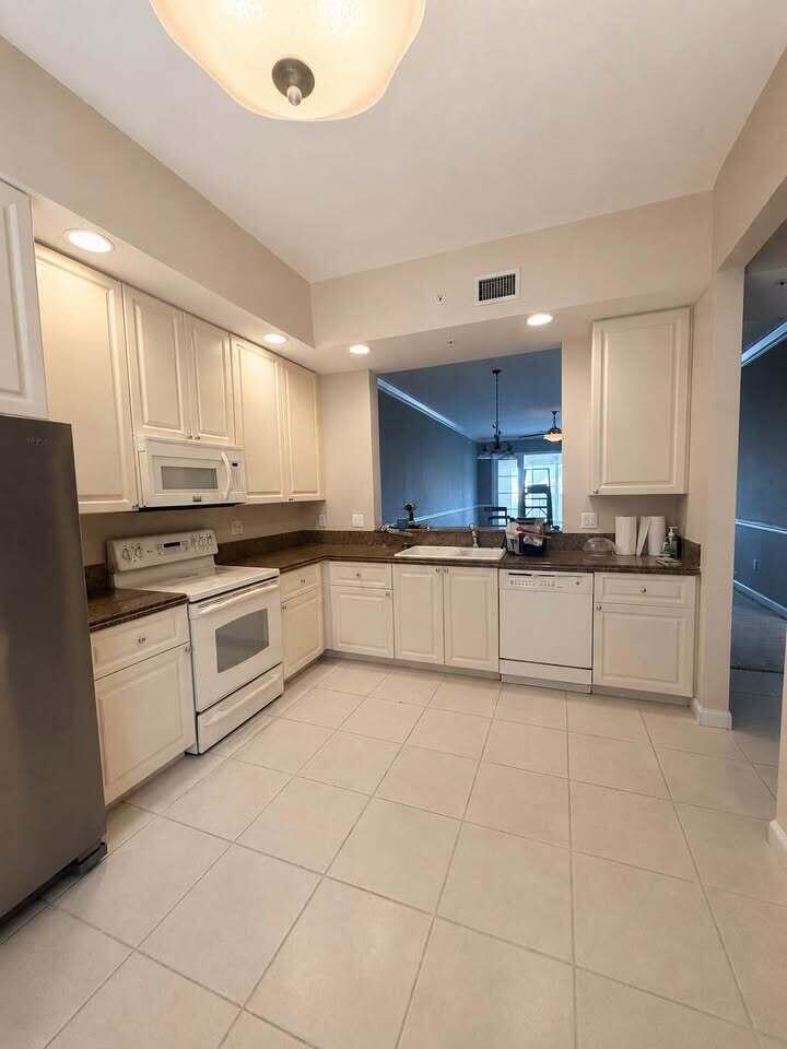 A kitchen with white cabinets, stainless steel appliances, dark countertops, and light-colored tile flooring — 5 Harbour Isle Drive E, Fort Pierce FL 34949, FORT PIERCE, FL