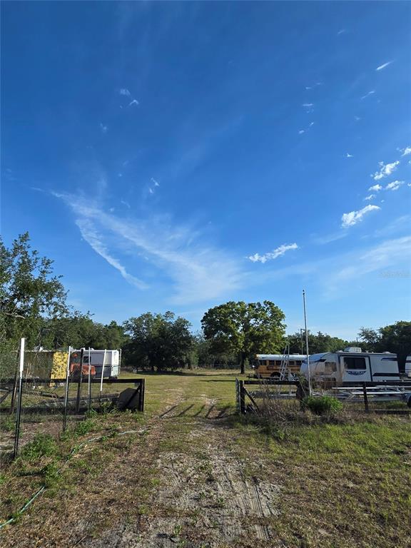 A dirt path leads through an open gate toward trees and parked vehicles — 14515 GIDDYUP LANE, HUDSON, FL