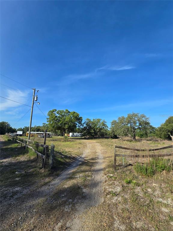 A dirt driveway leads through a wooden fence toward trees and vehicles on a lot — 14515 GIDDYUP LANE, HUDSON, FL