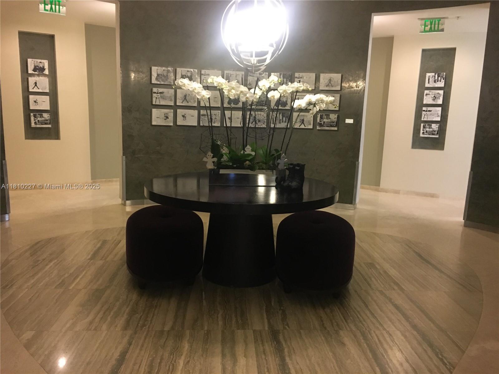 A circular dark wood table with two ottomans sits in a lobby with framed artwork — 10275 Collins Ave # 628, Bal Harbour FL 33154, BAL HARBOUR, FL