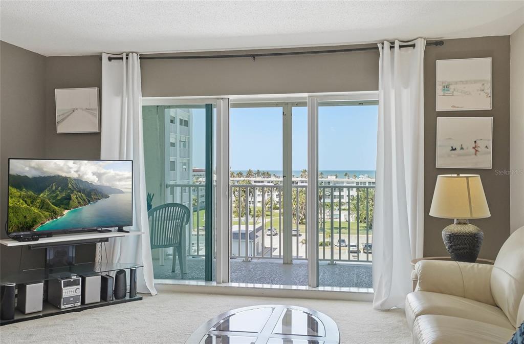 A living room features a television, a sliding glass door to a balcony, and ocean views — 420 64TH AVENUE UNIT 602, ST PETE BEACH, FL