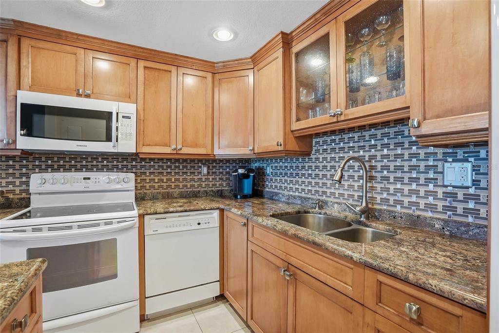 A kitchen features wood cabinets, granite countertops, a tile backsplash, and a white refrigerator — 420 64TH AVENUE UNIT 602, ST PETE BEACH, FL