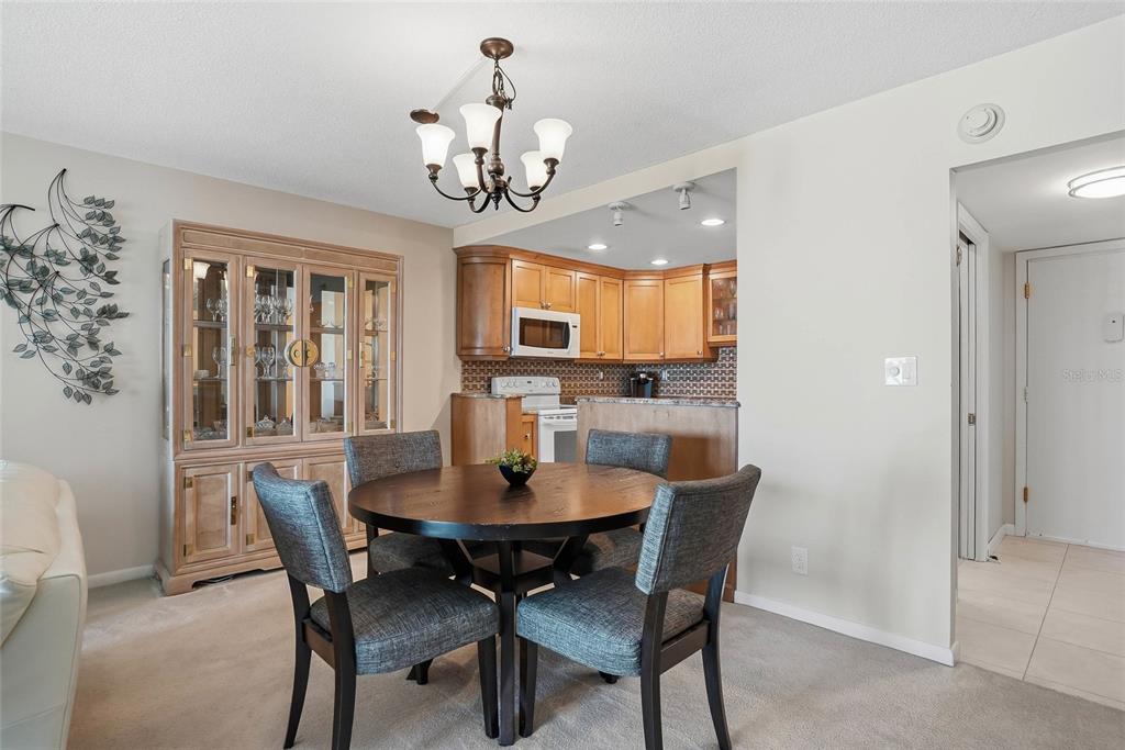 A kitchen features light wood cabinets, granite countertops, a tiled backsplash, and white appliances — 420 64TH AVENUE UNIT 602, ST PETE BEACH, FL