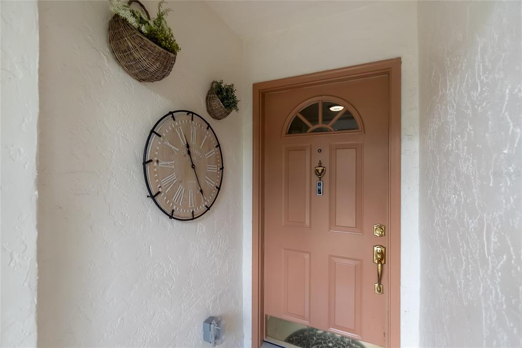 A salmon-colored front door with a clock and two wall baskets on the stucco wall — 4242 MADEIRA COURT UNIT 3315, SARASOTA, FL